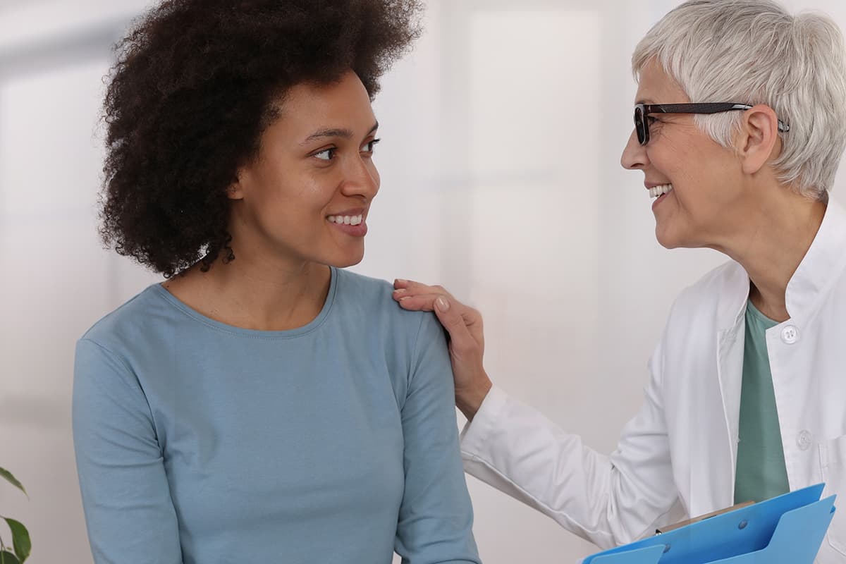 Young woman in a gray / blue top, smiling and talking to a senior woman who has her hand on her shoulder
