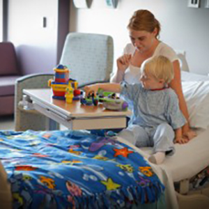 A female plays with a toddler at his hospital bed.