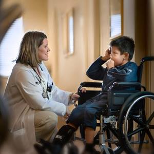 A female provider talks with a pediatric patient who is in a wheelchair.