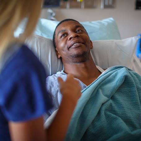 male-patient-hospital-bed-nurse-in-background