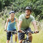 A man and woman in helmets are riding bicycles in the countryside.