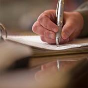 A hand holding a pen is writing information on a sheet of paper in a three ring binder