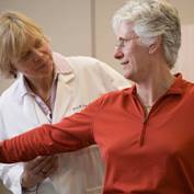 A female physician directs an older female patient as she raises her arms 