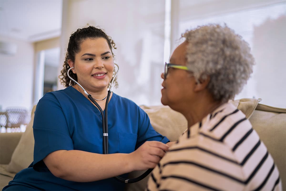 caregiver using a stethoscope to monitor the heartbeat of an old patient