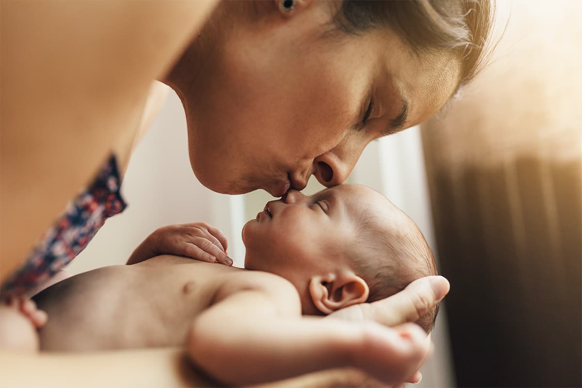 Woman leaning over a newborn baby and kissing their nose