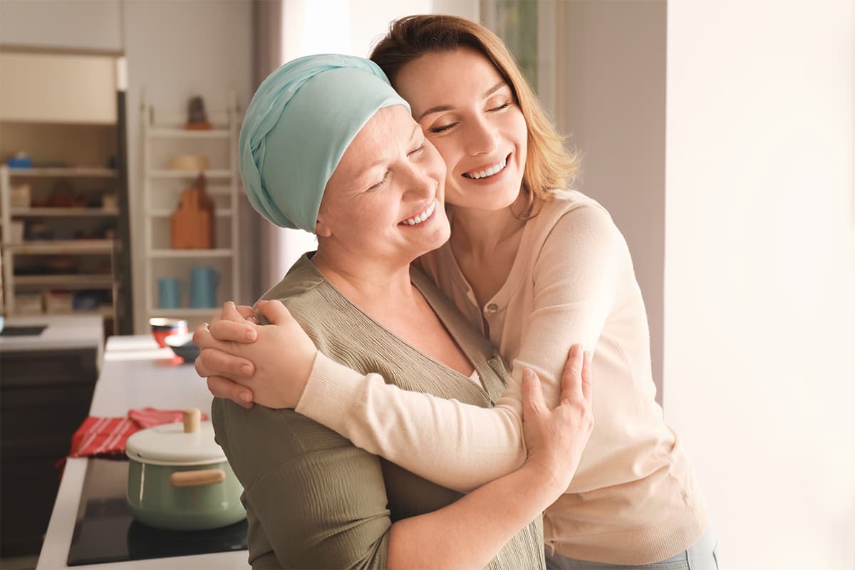 Older woman cancer patient hugged by her adult daughter