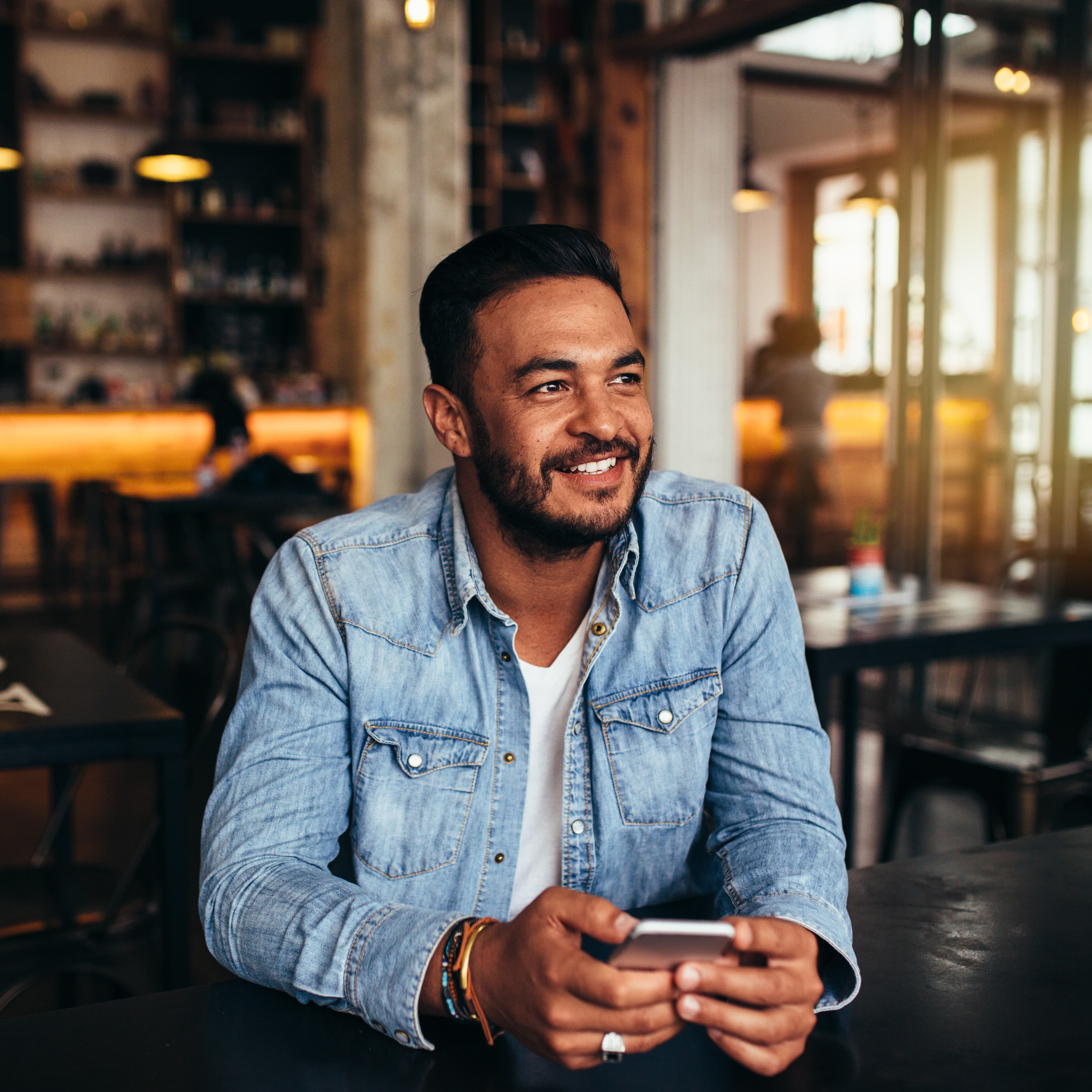 young man smiling sitting in restaurant holding his phone