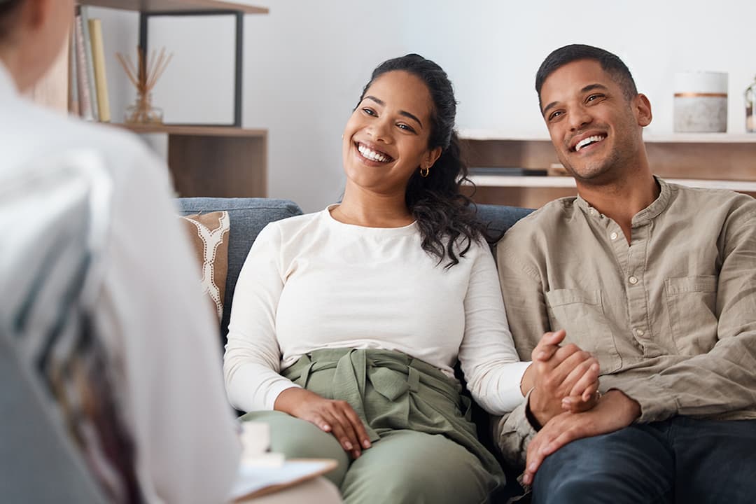 Smiling young man and woman holding hands on a sofa and talking to a medical professional