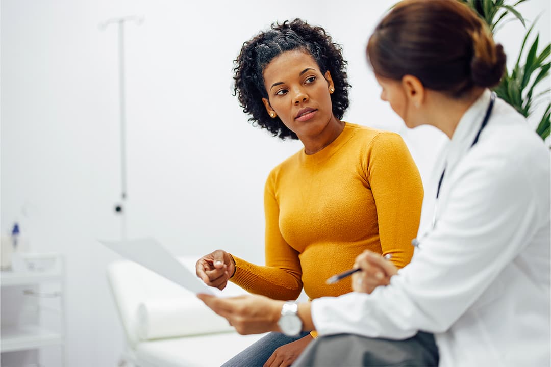 woman in an orange top discussing medical treatment with a doctor