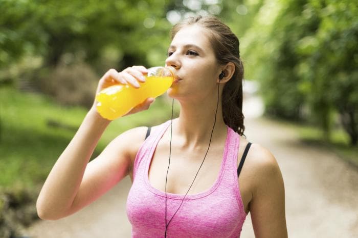 Woman in exercise clothes drinking orange juice outside