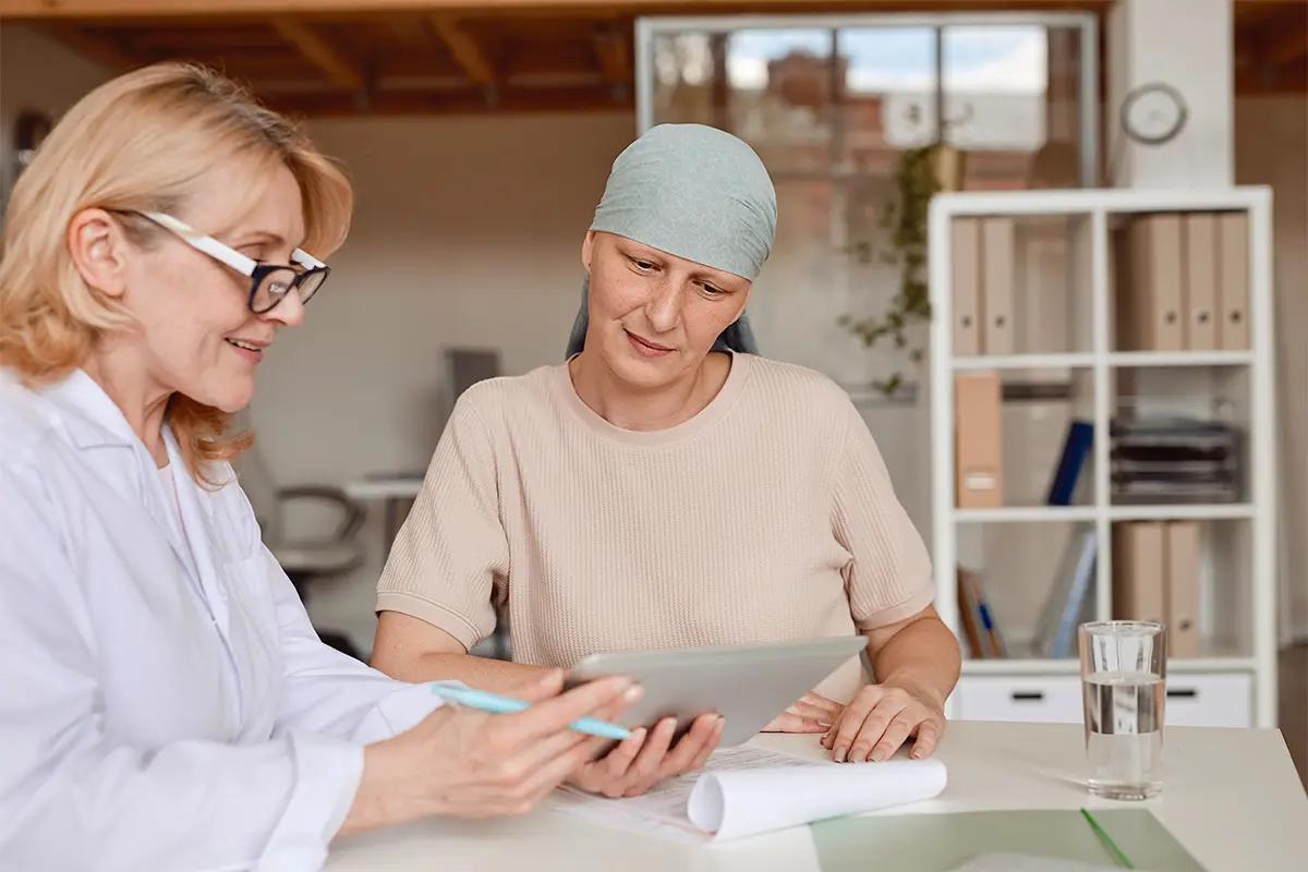 Woman in a blue headband sitting and talking to a doctor who is showing her something on a tablet