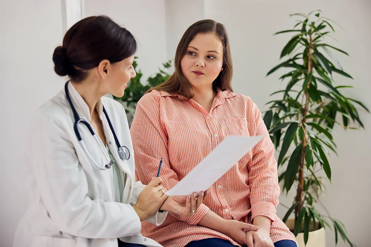 Woman in a pink top talking to a doctor who is showing her a document