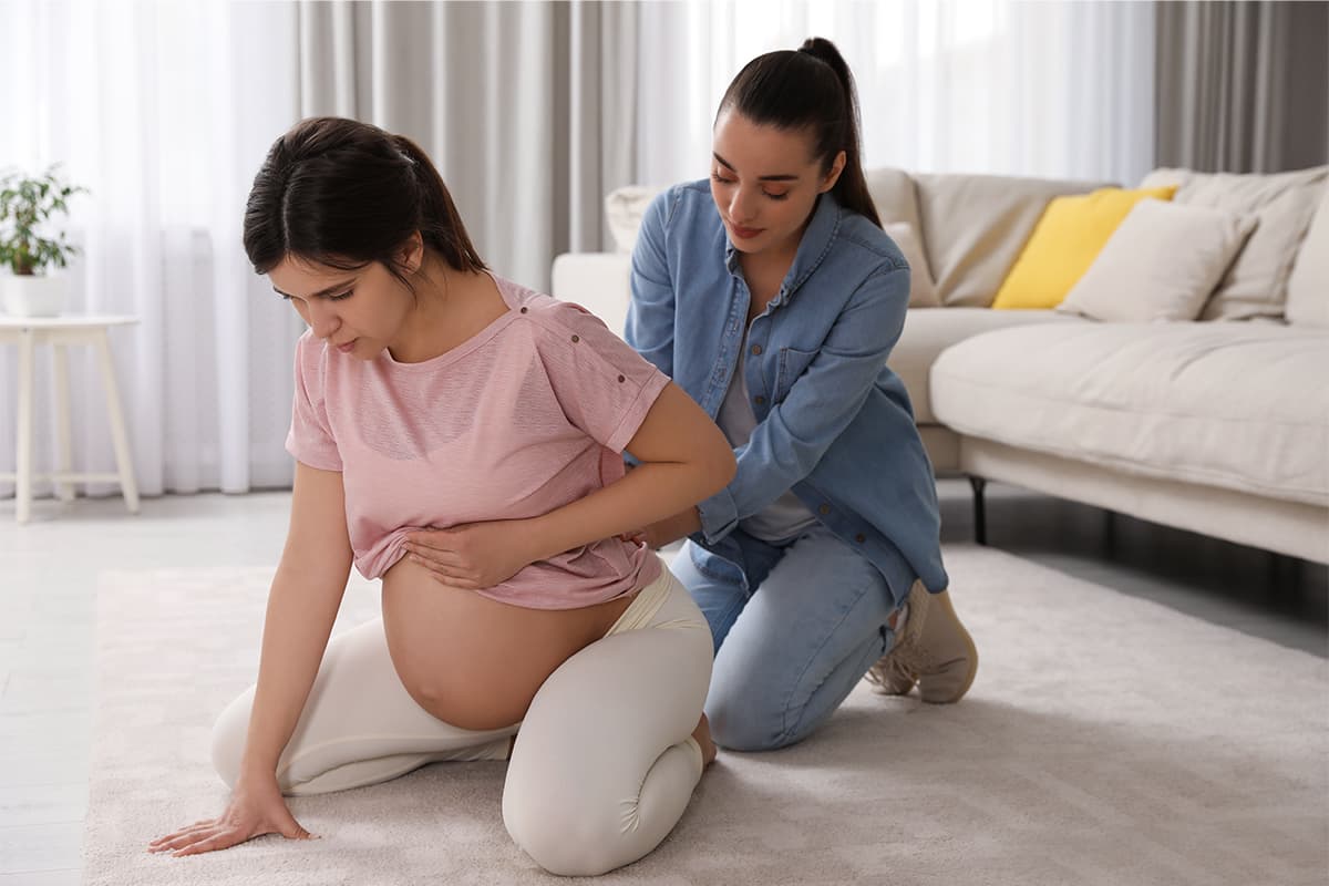 Woman in labor at home, kneeling with someone supporting her behind