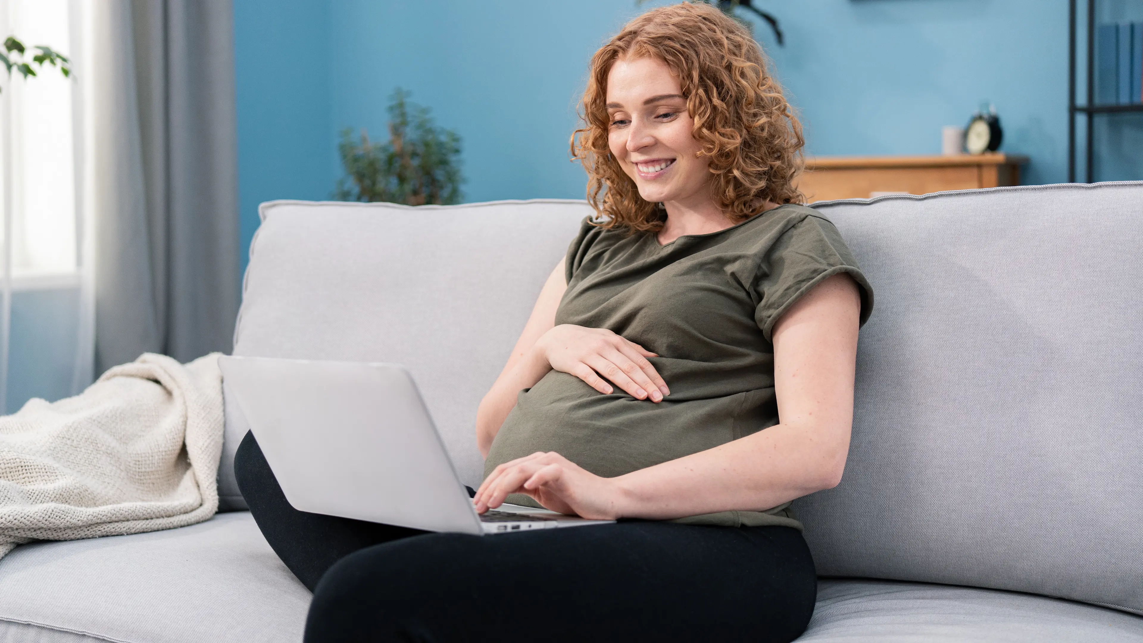 A pregnant woman sitting on a couch using a laptop