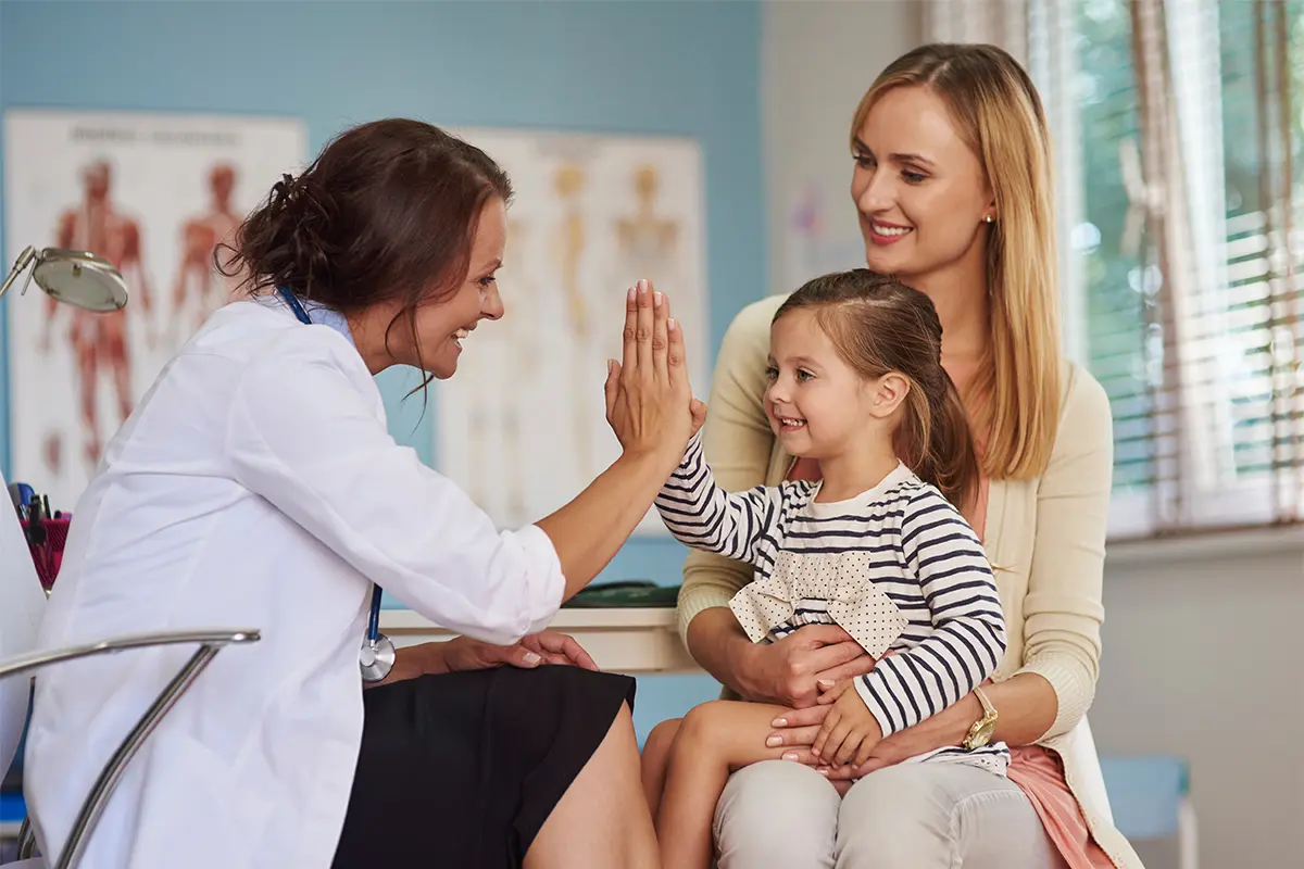 Little girl high fiving a doctor while sitting on her mother's lap