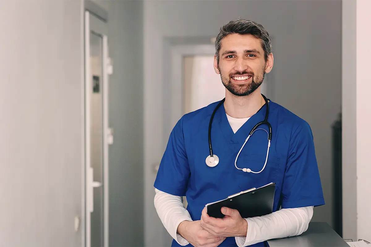 Man in blue scrubs with a stethoscope and a clipboard