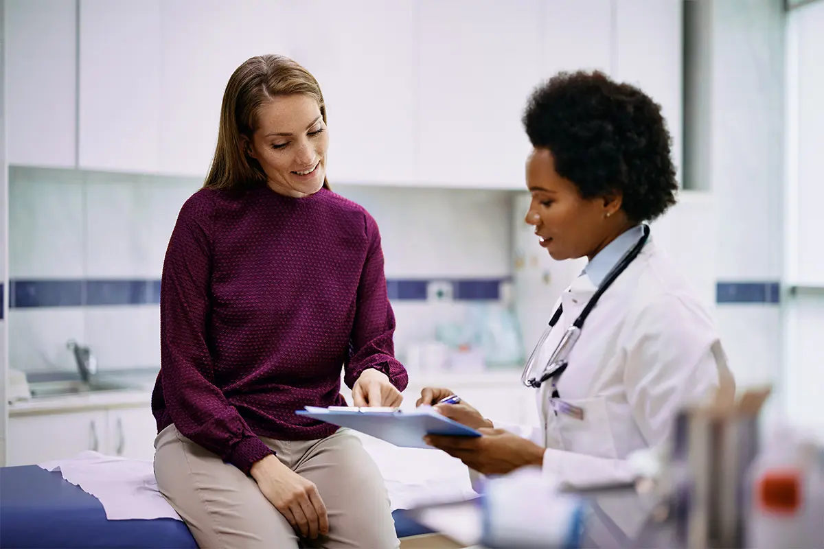 Woman in a dark red top sitting in a consultation room talking to a doctor holding a chart